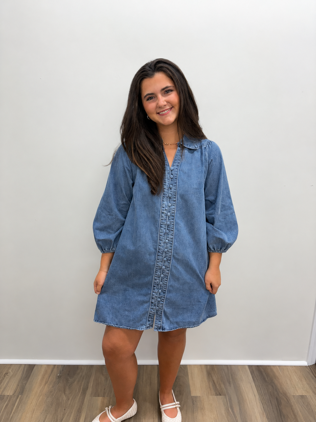 Women’s medium-wash denim mini dress featuring a collared neckline, button-front closure, three-quarter-length puff sleeves with elastic cuffs, and a relaxed A-line silhouette.