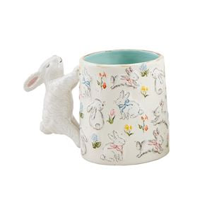 A easter bunny mug with flowers and bunnies all over with a bunny as the handle.