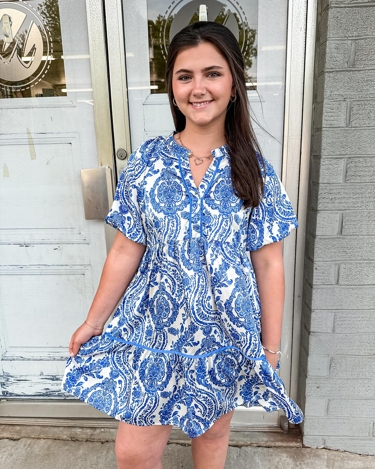 Allona dress with a smocked v-neckline and puff short sleeves in a blue and white design.