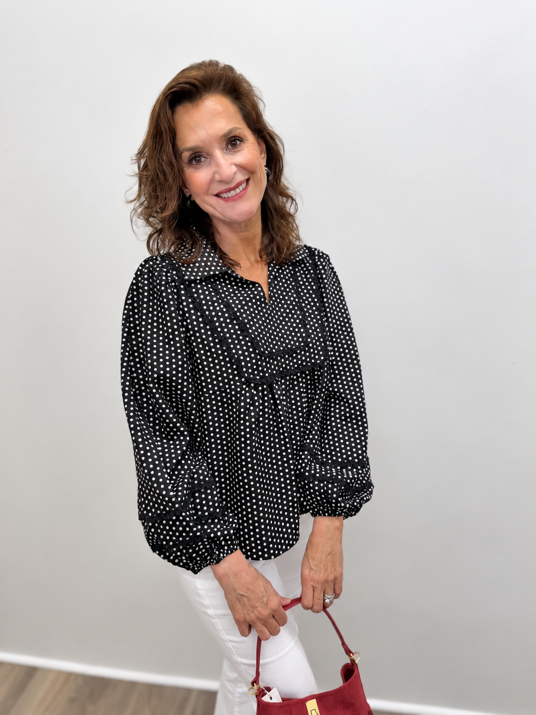 Women’s black blouse featuring an allover white polka dot print, oversized ruffle bib collar, and long balloon sleeves with layered ruffle details.