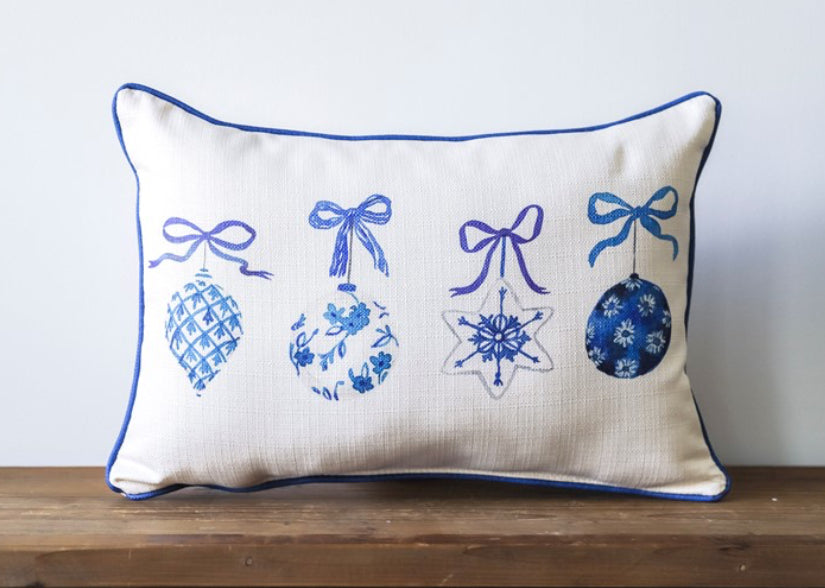 A cream pillow with an assortment of 4 blue ornaments with bows at the tops.