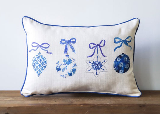 A cream pillow with an assortment of 4 blue ornaments with bows at the tops.