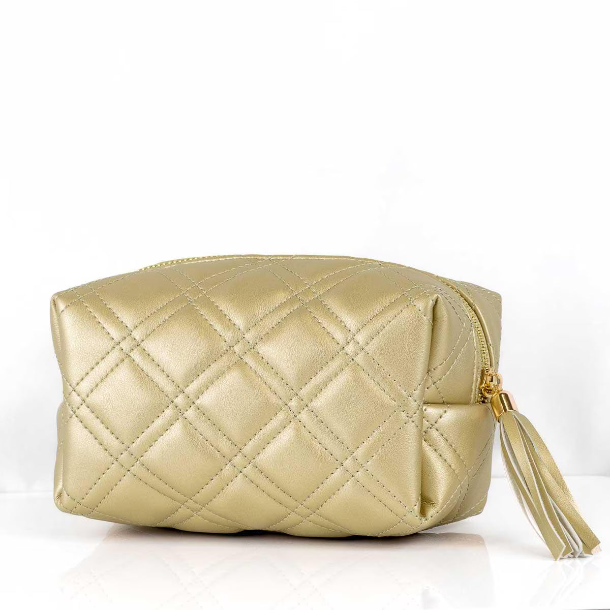 A metallic gold quilted cosmetic pouch with a diamond pattern, gold zipper, and a matching tassel, shown on a white reflective surface against a white background.