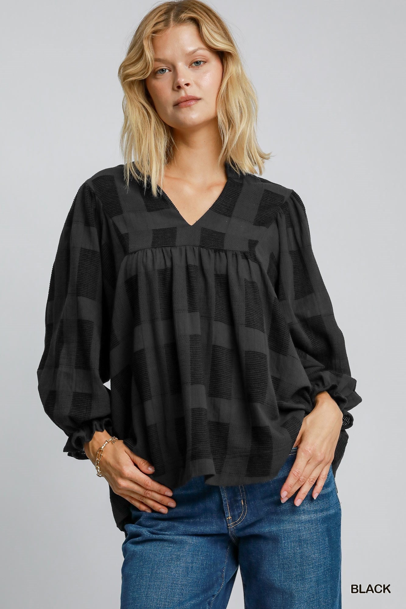 A long-sleeved black blouse with a checkered pattern. It features a V-neckline and gathered detailing at the front, creating a loose, flowy fit.