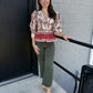 This top is a romantic, vintage-inspired blouse with a detailed, feminine design:

Ivory/cream base with an intricate red, burgundy, olive, and green floral/ornamental print
V-neckline with delicate lace-like trim
Long sleeves with gently gathered, puffed shoulders and fitted cuffs
Button-front closure through the bodice
Defined waist with a flattering, slightly fitted shape
A striking red printed border along the lower portion
Scalloped lace trim along the hem and sleeve cuffs
Slightly peplum-like shape at