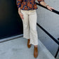 The pants are cream-colored cropped jeans with a relaxed, polished silhouette:

Warm ivory/cream denim that pairs beautifully with the navy floral top
Mid- to high-rise fit with a classic five-pocket jean construction
Straight-leg to gently flared silhouette through the hips and legs
Cropped length, hitting just above the ankle
Raw/frayed hems that add a casual, contemporary touch
Clean, minimal finish without heavy distressing