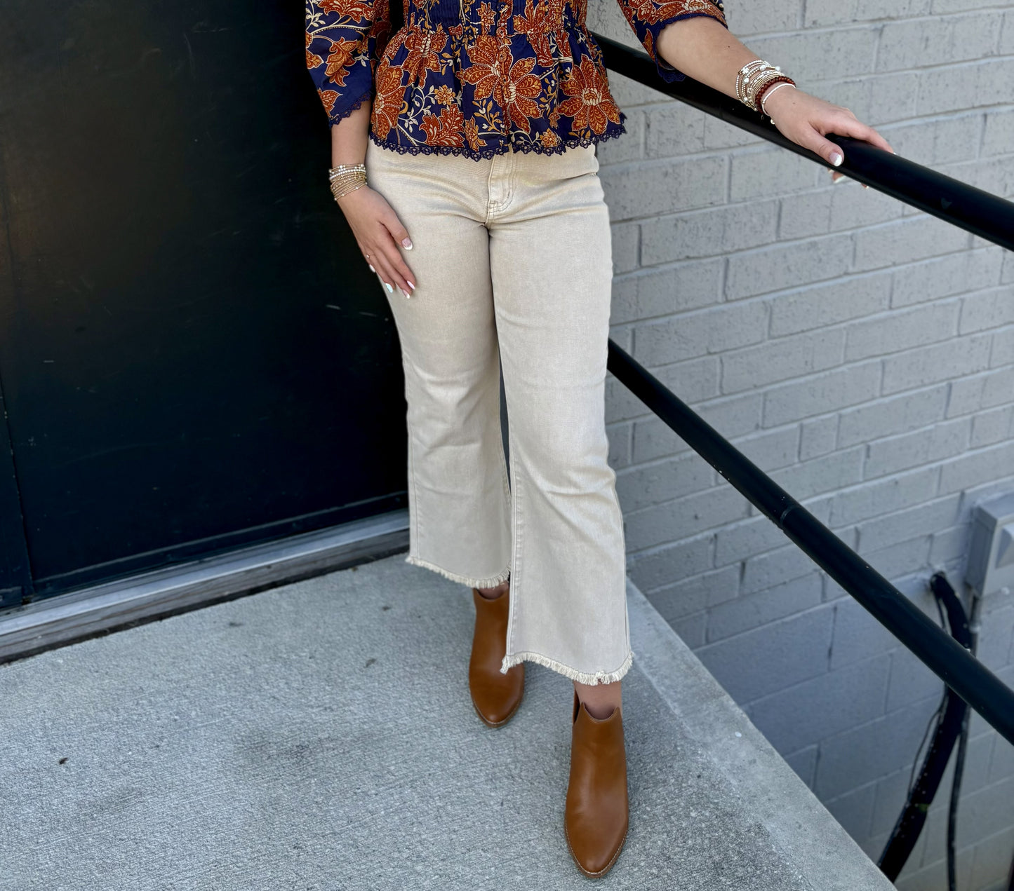 The pants are cream-colored cropped jeans with a relaxed, polished silhouette:

Warm ivory/cream denim that pairs beautifully with the navy floral top
Mid- to high-rise fit with a classic five-pocket jean construction
Straight-leg to gently flared silhouette through the hips and legs
Cropped length, hitting just above the ankle
Raw/frayed hems that add a casual, contemporary touch
Clean, minimal finish without heavy distressing