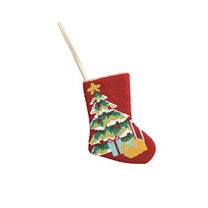 A red Christmas stocking ornament with a hand-painted style green Christmas tree, gold star, and wrapped presents, hanging from a wooden stick on a white background.