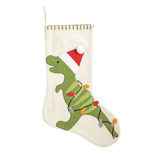 An off-white Christmas stocking featuring a green embroidered dinosaur wearing a red Santa hat, with colorful string lights wrapped around it, shown against a plain white background.