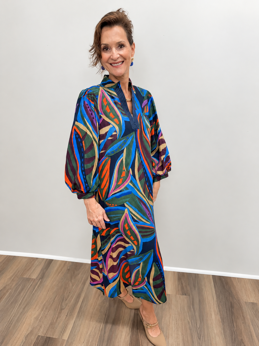 Women’s midi dress featuring a bold abstract leaf print in navy, royal blue, green, orange, purple, and tan, with a V-neckline and three-quarter-length balloon sleeves.