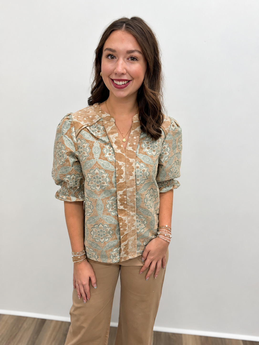 Women’s tan and sage green medallion print blouse featuring a V-neckline, contrast patterned trim, and short puff sleeves with smocked cuffs.