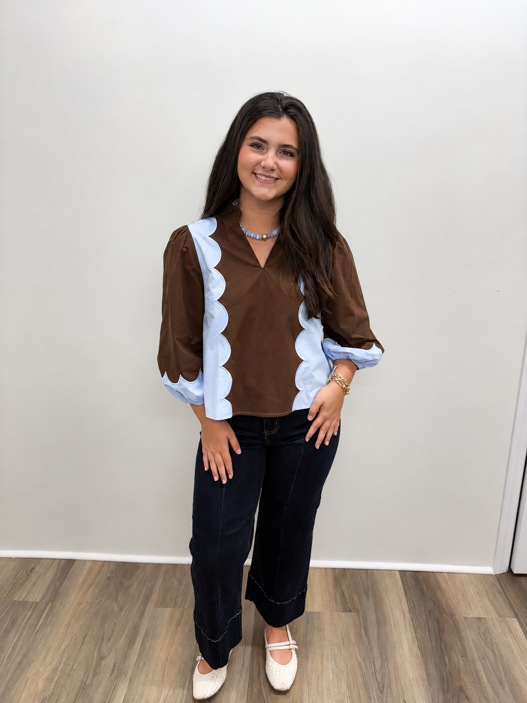 Brown blouse featuring light blue scalloped trim along the front and sleeves, a V-neckline, and three-quarter puff sleeves.