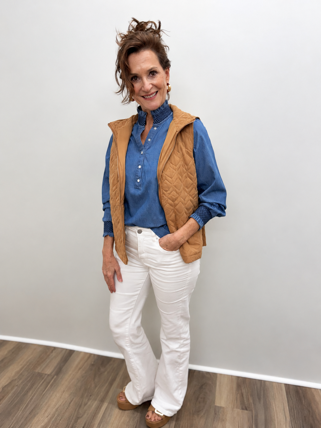 Women’s blue chambray blouse featuring a button-front neckline, ruffled high collar, long balloon sleeves, and dark blue smocked detailing at the collar and cuffs.