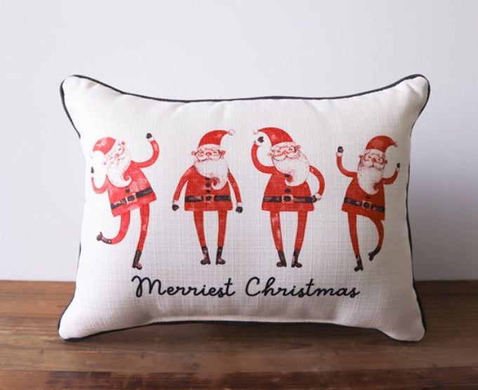 A cream pillow with four Santa's dancing with the words "merriest Christmas" written in cursive at the bottom. 