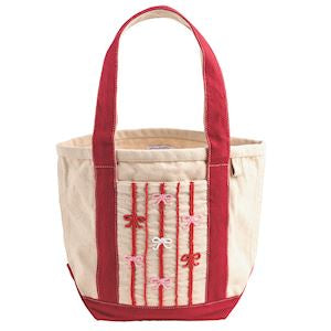 A canvas tote bag with a cream-colored body, red trim, and embroidered red and pink bow details on the front pocket, set against a plain white background.