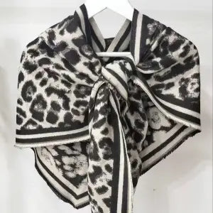 Leopard-print scarf with black, white, and gray tones, featuring a striped border and a knotted center. The scarf is displayed hanging on a white hanger against a light background.