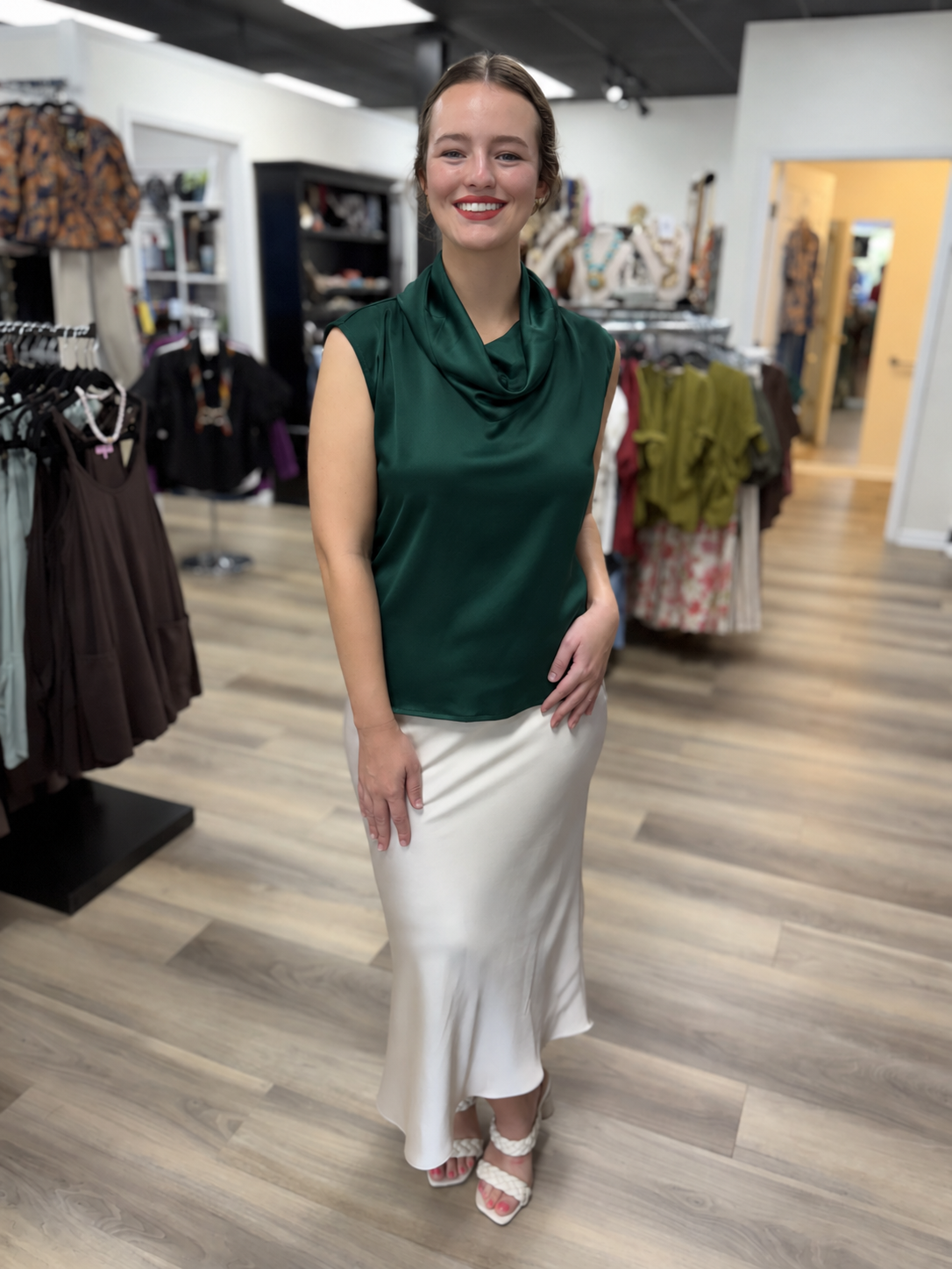 This top is an elegant deep green satin blouse with a soft, lustrous finish. It features a sleeveless silhouette with extended shoulders and a beautifully draped cowl neckline that creates a sophisticated, fluid look. The relaxed, straight-cut bodice falls smoothly over the figure, while the rich wine-red color gives it a polished, dressy feel perfect for work, dinners, or special occasions.