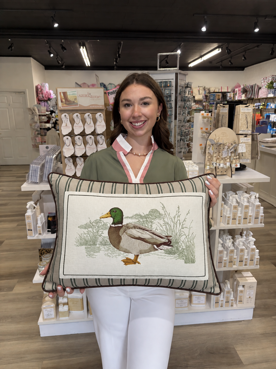 This decorative rectangular duck pillow features a detailed mallard duck illustration surrounded by soft, sketched marsh grasses and foliage. The center panel has a natural cream background, while the outer border features neutral beige and muted green stripes for a classic, outdoors-inspired look. Finished with dark brown piping around the edges, this pillow has a charming lodge-style feel that's perfect for a den, living room, cabin, or nature-inspired space.