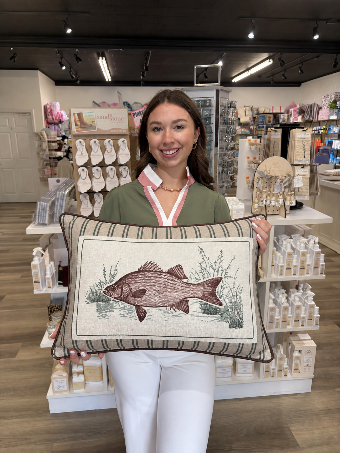 This decorative rectangular fish pillow features a detailed, vintage-inspired fish illustration surrounded by delicate aquatic grasses and water accents. The cream center panel is framed by a neutral striped border in beige, taupe, and muted green, giving it a classic outdoorsy look. Finished with dark brown piping around the edges, this pillow is perfect for adding a rustic, lodge-inspired touch to a living room, lake house, cabin, or den.