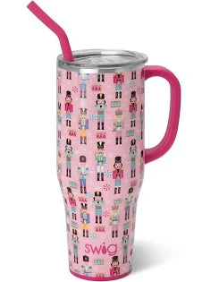 A Swig Christmas 30oz tumbler with a lid and straw. The body of the tumbler features colorful nutcrackers in various outfits. These nutcrackers are arranged in a grid-like pattern against a pink background.