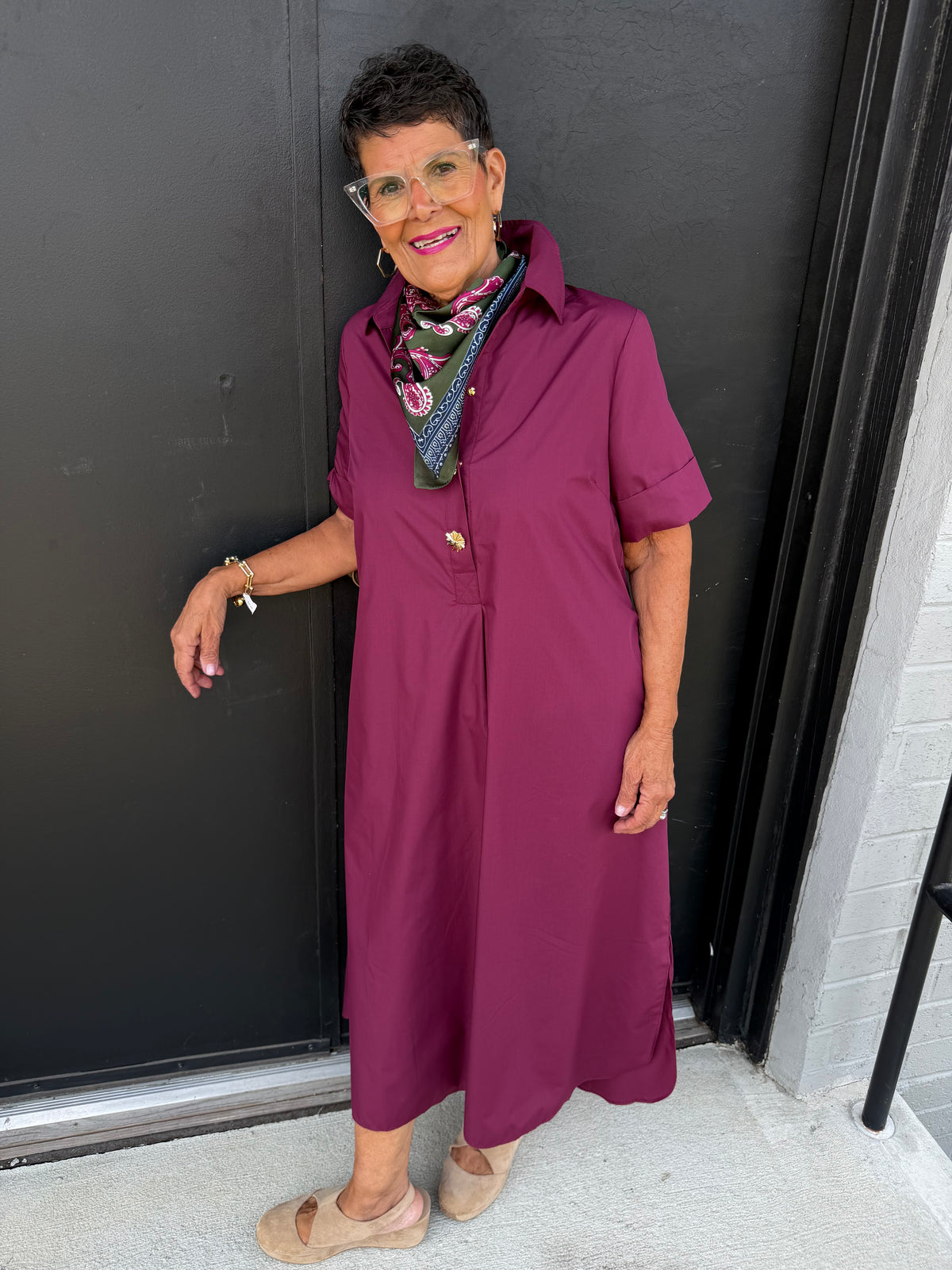 This is a sophisticated, relaxed-fit shirt dress in a rich berry-plum color, with a classic silhouette and polished details.

Color: Deep berry, plum, or mulberry—a rich jewel tone that feels elegant and versatile.
Neckline: Traditional pointed shirt collar with a neat, structured finish.
Front: Partial button-front closure with decorative gold-tone buttons that add a refined accent.
Sleeves: Short sleeves with a slightly structured, cuff-like folded finish.
Silhouette: Relaxed and comfortably loose through