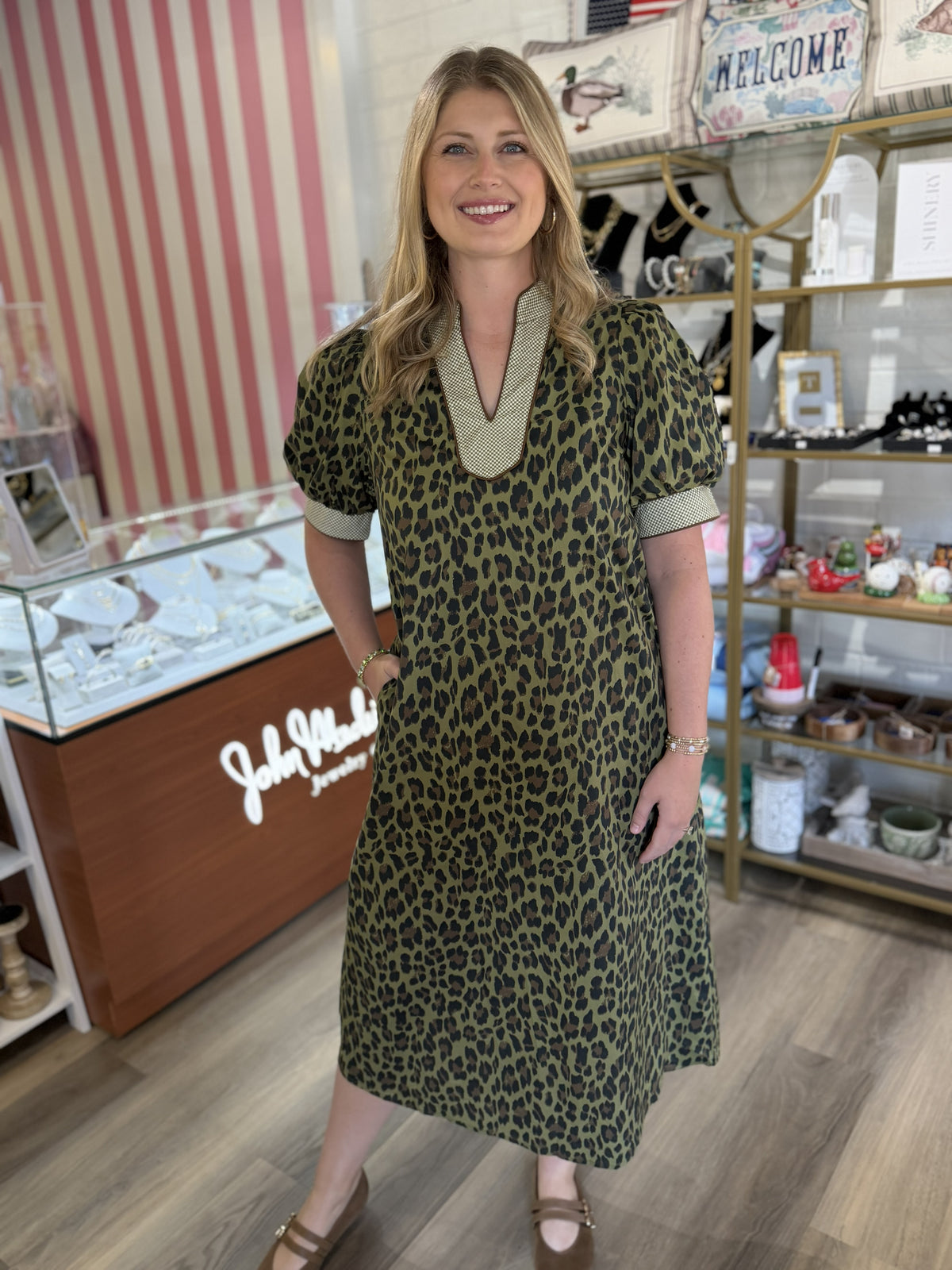 This olive green midi dress features a bold allover leopard print for a chic, statement-making look. It has a relaxed A-line silhouette with feminine puff short sleeves and contrasting patterned trim at the cuffs. The standout neckline features a deep V-shaped split with a wide coordinating contrast border that adds an elevated touch. Side pockets complete the look with everyday functionality. A fun, effortless dress that pairs perfectly with flats, sandals, or boots.