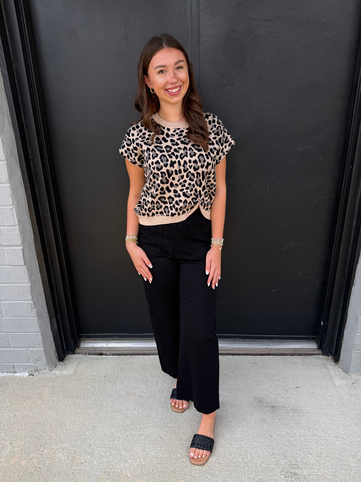 This is a chic leopard-print knit top with a feminine twisted-front detail and contrast trim.

Print: Classic leopard print in black, warm beige, and cream tones.
Neckline: Simple round crew neckline with a contrasting cream-colored ribbed edge.
Sleeves: Short, slightly relaxed cap sleeves, giving it an easy, polished shape.
Fit: Comfortable and gently fitted through the bodice without feeling overly tight.
Hem: The standout feature is the twisted/gathered center-front hem, creating a subtle sweetheart-like