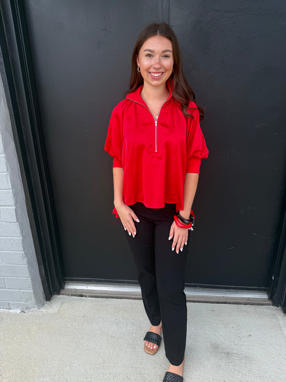 This is a bright red, relaxed-fit pullover top with sporty details and a polished twist.

Color: Vivid cherry/red.
Neckline: A stand-up funnel/zip collar with a short silver zipper extending down the center front.
Sleeves: Loose short-to-three-quarter sleeves with gathered volume and fitted ribbed cuffs at the elbows.
Fit: Oversized and flowy through the body, creating an easy, comfortable silhouette.
Hem: Curved, slightly longer at the sides/back, giving it a subtle tunic effect.
Fabric: Smooth, lightweigh