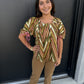 This top features a soft, flowing silhouette with a retro-inspired geometric print. It has:

Multicolor chevron/zigzag pattern in olive green, brown, blush pink, cream, and tan
Rounded scoop neckline with subtle gathering at the center
Short, voluminous sleeves with adjustable pink tie details at the cuffs
Relaxed, slightly flared fit that drapes away from the body
Lightweight, textured fabric that gives the top an airy, effortless feel
A slightly longer length that pairs easily with slim or straight-leg bo