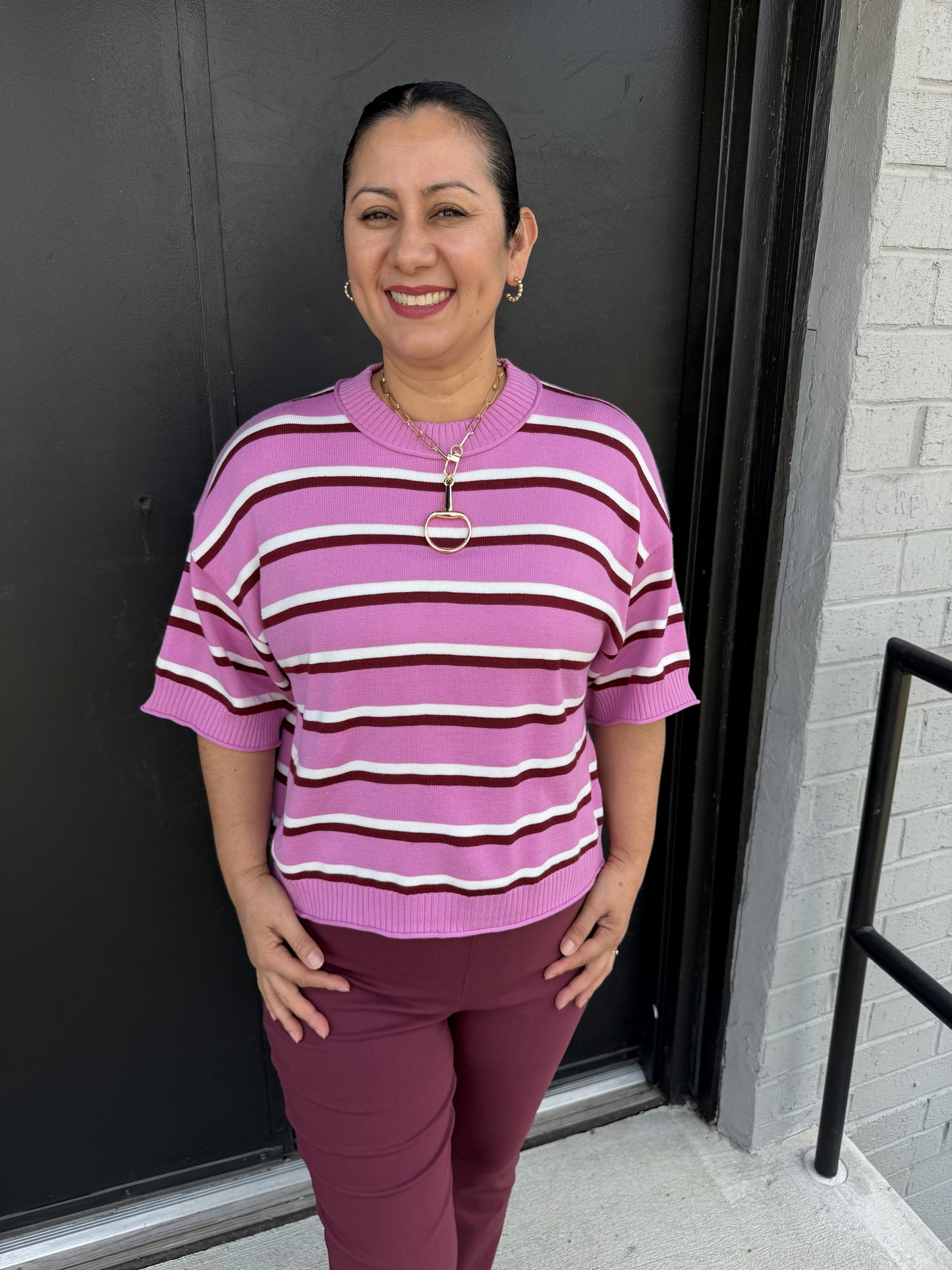 This sweater is a pretty, polished knit with a playful retro feel:

Soft pink/lilac base color with horizontal stripes in burgundy and ivory
Classic crew neckline with a ribbed collar
Short, relaxed sleeves with ribbed cuffs
Easy, slightly boxy fit that drapes comfortably without being oversized
Ribbed hemline for a finished, structured look
Lightweight knit appearance makes it an easy transitional-season layering piece
The pink and burgundy palette gives it a feminine, sophisticated pop of color