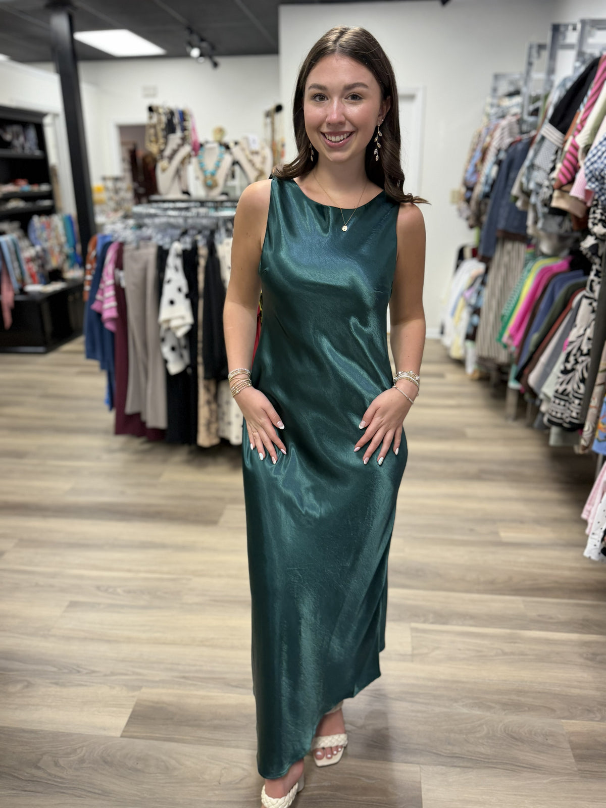 This is a rich emerald green satin maxi dress with an elegant, fluid silhouette. The lustrous fabric has a beautiful sheen that catches the light, giving the dress a sophisticated, dressy finish.

It features a sleeveless design with a softly rounded bateau neckline in front and a striking low scoop back with a draped cowl detail. The dress skims the figure before falling into a relaxed, flowing ankle-to-maxi length hem. Minimalist yet glamorous, it’s a beautiful option for weddings, formal events, holiday 