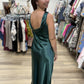 This is a rich emerald green satin maxi dress with an elegant, fluid silhouette. The lustrous fabric has a beautiful sheen that catches the light, giving the dress a sophisticated, dressy finish.

It features a sleeveless design with a softly rounded bateau neckline in front and a striking low scoop back with a draped cowl detail. The dress skims the figure before falling into a relaxed, flowing ankle-to-maxi length hem. Minimalist yet glamorous, it’s a beautiful option for weddings, formal events, holiday 