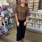 This is a rich chocolate brown short-sleeve top with a soft, suede-like texture and relaxed silhouette. It features a round neckline with contrasting rust-brown ribbed trim, subtle gathering across the front, and short puff sleeves with softly gathered shoulders for a feminine touch. A delicate ruffled trim along the hemline adds extra detail. The warm neutral color and textured finish make it an easy fall staple that pairs beautifully with denim, skirts, or trousers.
