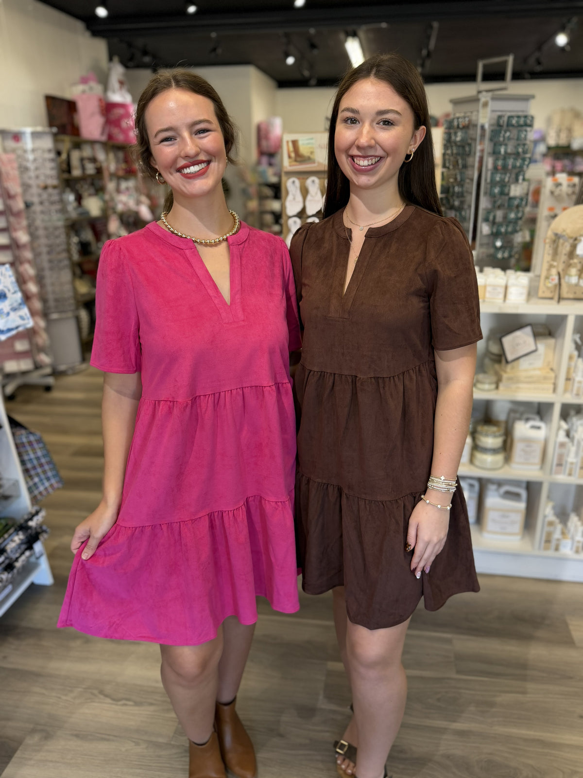 This is a rich chocolate brown tiered dress with a soft, suede-like texture and an easy, relaxed silhouette. It features a split V-neckline, short sleeves with subtle gathering at the shoulders, and a gently gathered waist seam. The skirt flows into tiered sections with a ruffled hem, creating a feminine, slightly flared shape that falls above the knee.