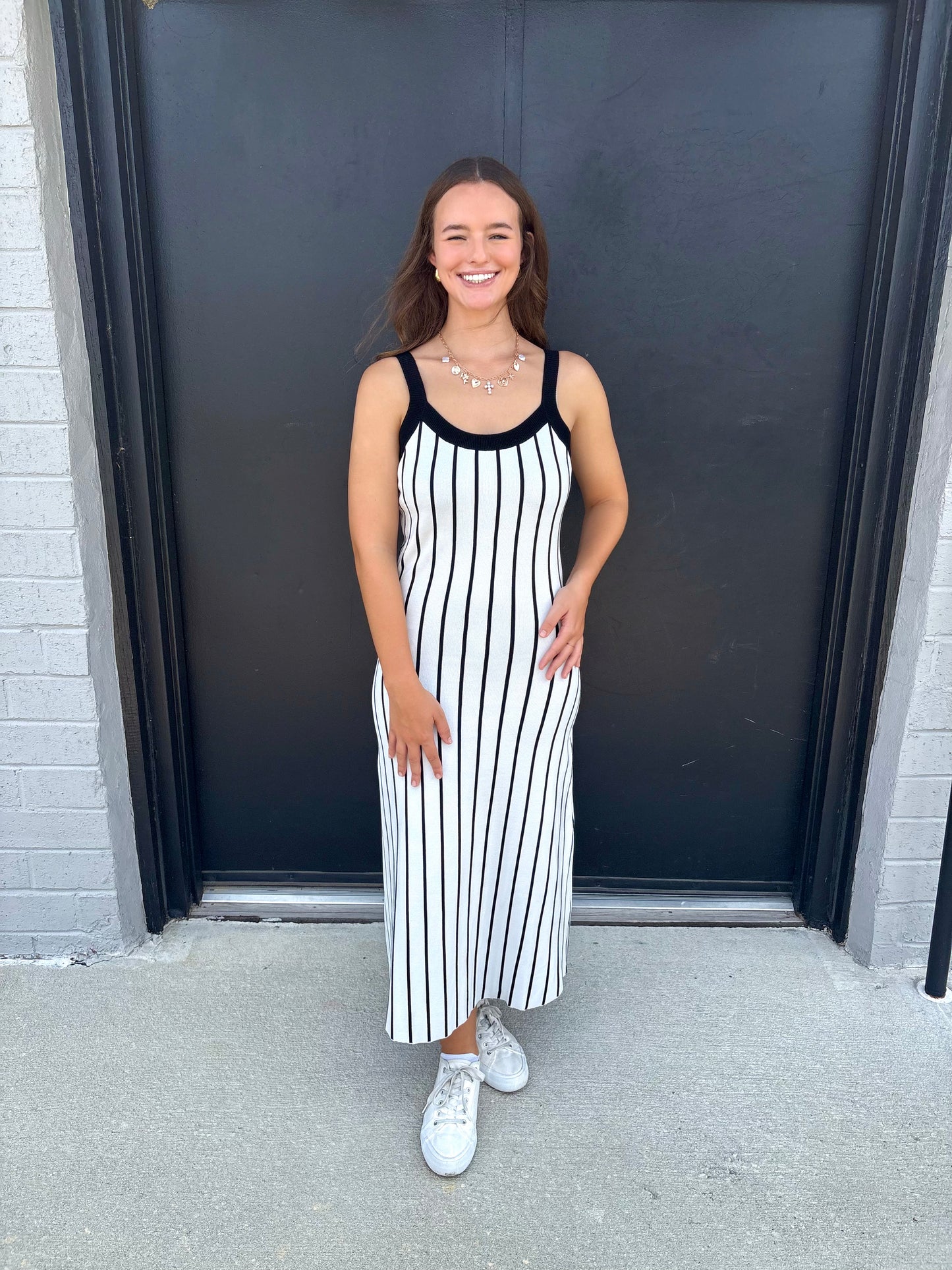 Woman wearing a black and white striped dress standing in front of a dark door.