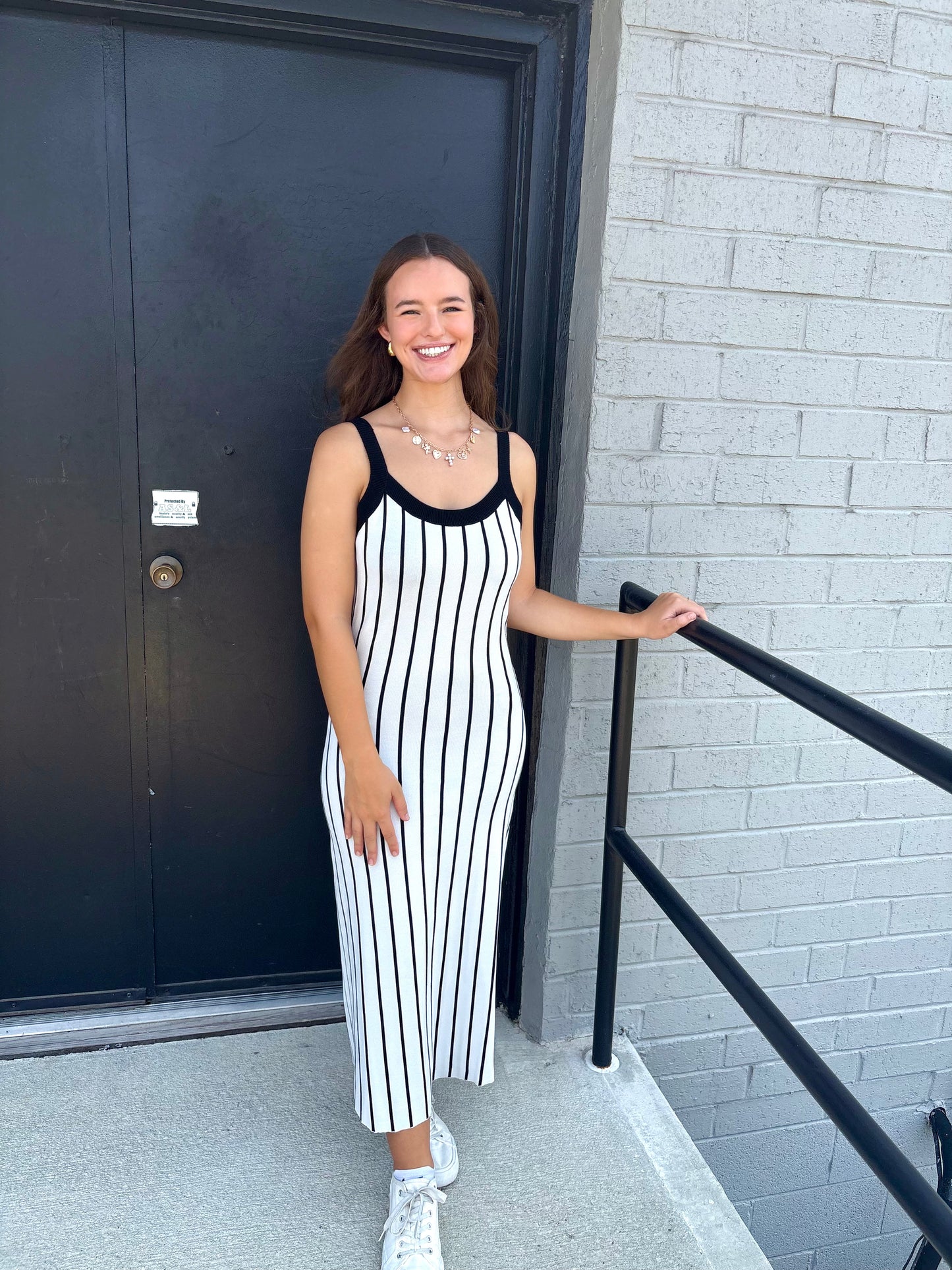 Woman in a black and white striped dress standing outside a building.