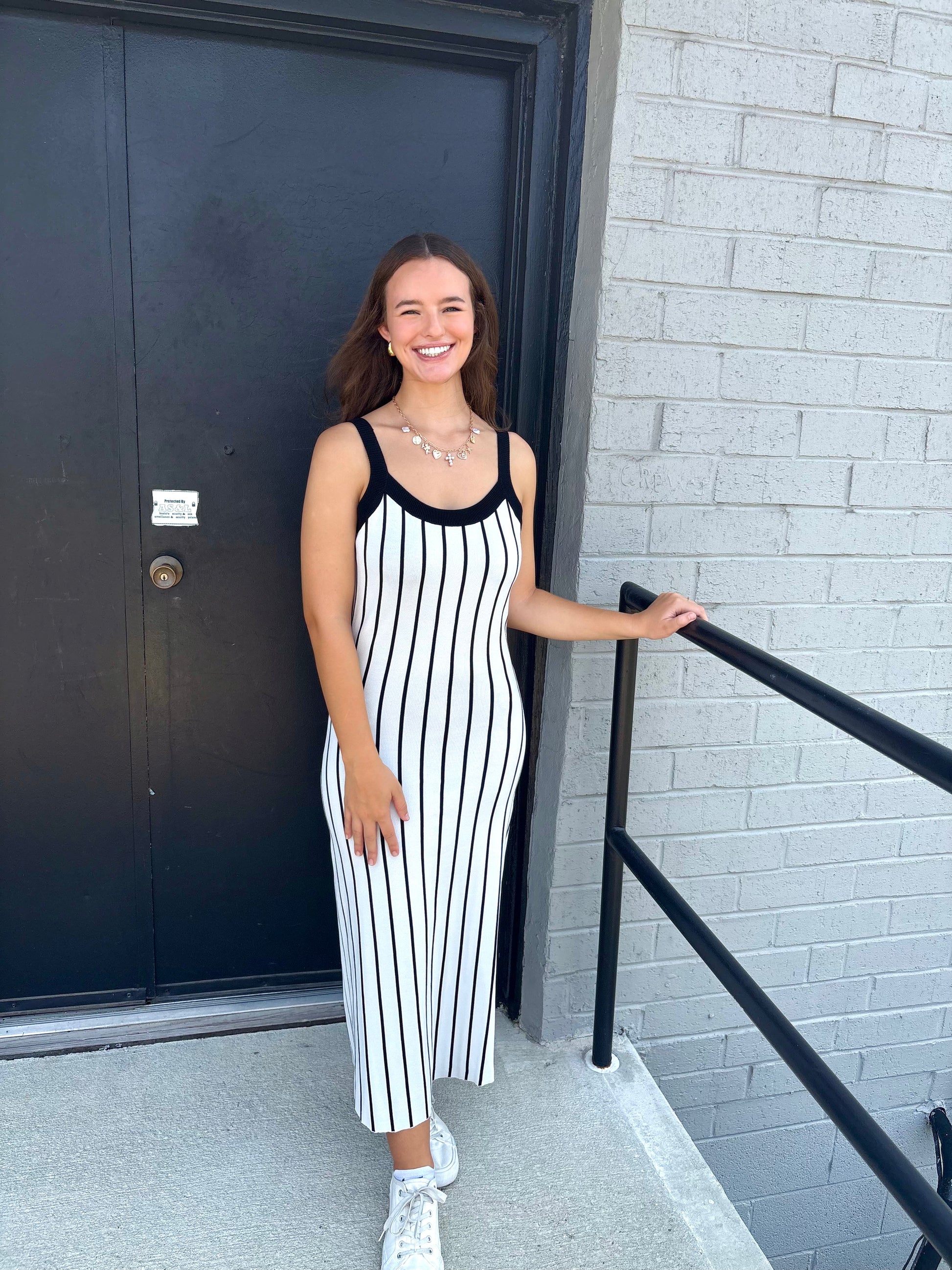 Woman in a black and white striped dress standing outside a building.