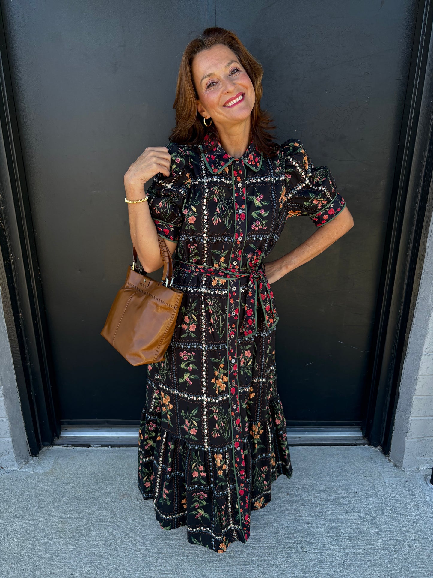 Woman in a floral dress holding a brown bag against a dark background