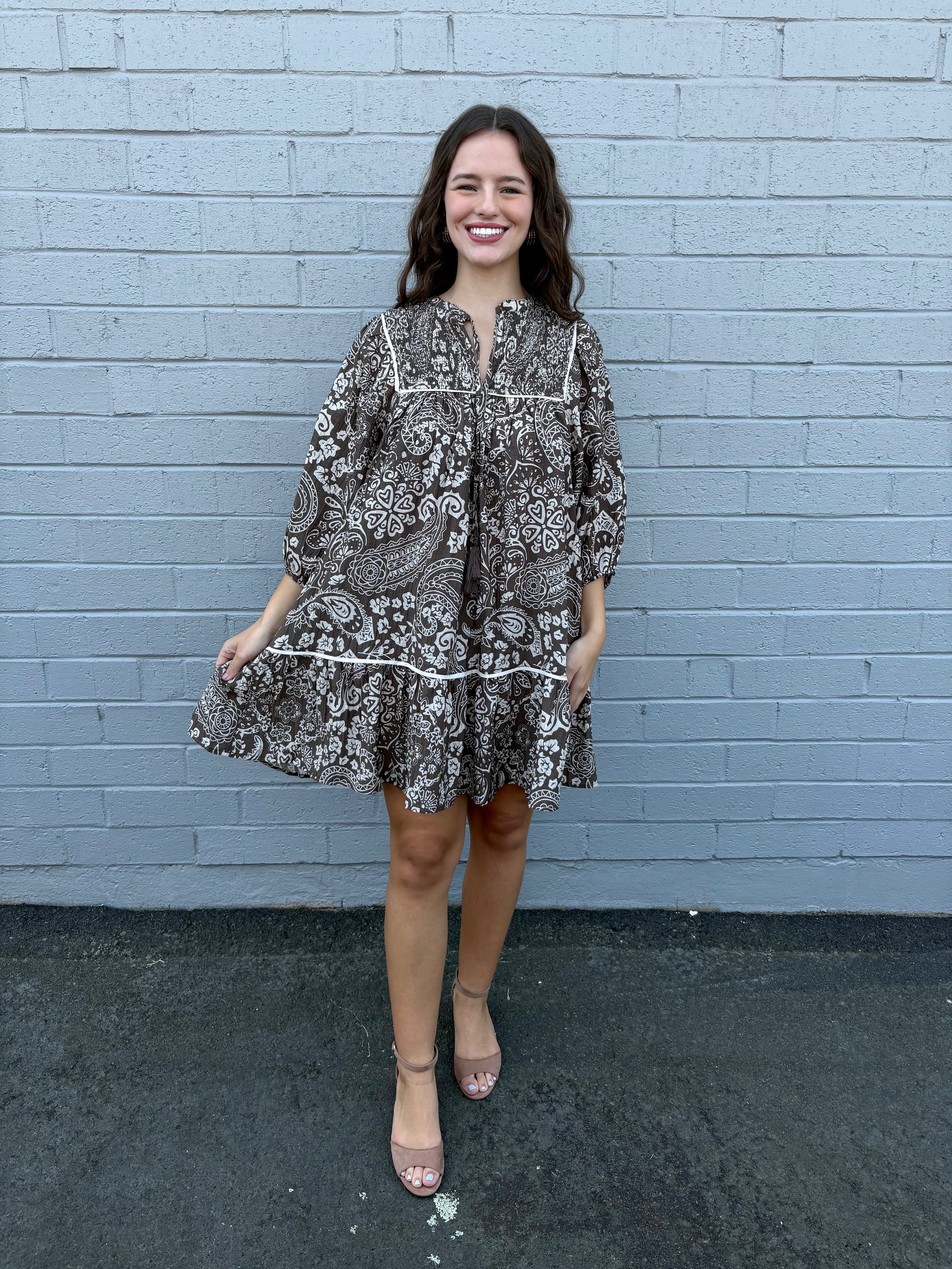 Woman wearing a patterned dress standing against a light blue brick wall.