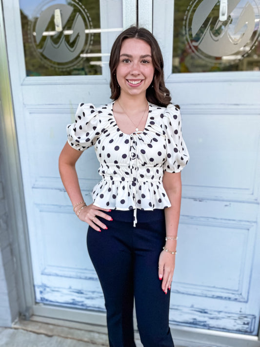 A black and white polka dot top with puff sleeves and an elastic waist and scoop neck design.