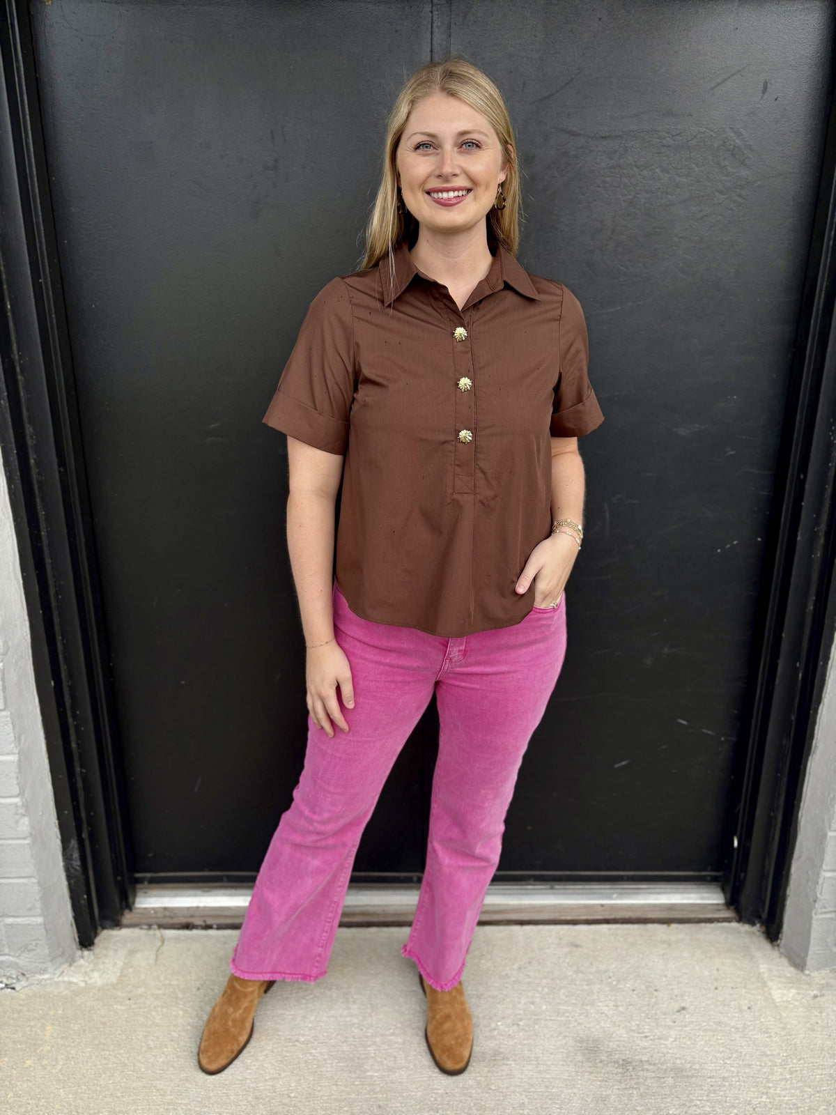 This is a chocolate-brown short-sleeve button-front blouse with a polished, slightly retro boutique feel.

Color: Rich chocolate brown with a warm, earthy tone.
Collar: Classic pointed shirt collar for a tailored look.
Front: Partial button-front closure featuring decorative gold-tone floral buttons, which add a feminine statement detail.
Sleeves: Short sleeves with wide, structured cuffs that give the blouse a crisp finish.
Fit: Relaxed and easy through the body, with a gently straight silhouette that can 