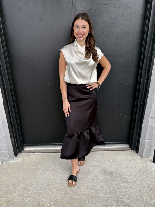 This is a sleek black satin midi skirt with a dramatic ruffled mermaid hem.

Color: Classic deep black with a subtle satin sheen.
Silhouette: Slim and streamlined through the waist, hips, and upper legs, creating an elegant column shape.
Waist: Clean, high-rise waistband with a smooth, fitted finish.
Length: Midi length, falling below the knee and toward mid-calf.
Hem: The standout detail is the voluminous flounced/ruffled hem, which begins around the lower calf and creates a beautiful flare and movement.
F