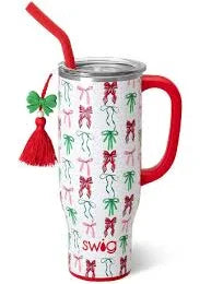 A Swig Christmas 30oz tumbler with a lid and a straw and decorative red tassel with green bow on the side. The tumbler features a pattern of red bows and green bows on a white background.