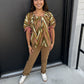 The pants are classic tan/camel-colored trousers with a polished yet relaxed feel. They feature:

Warm camel/taupe color
Mid- to high-rise waistband
Straight-leg silhouette with a comfortable, easy fit
Full-length cut with the hems casually rolled/cuffed
Clean, minimal styling with a smooth, structured appearance
Versatile neutral shade that pairs beautifully with the earthy tones in the printed top