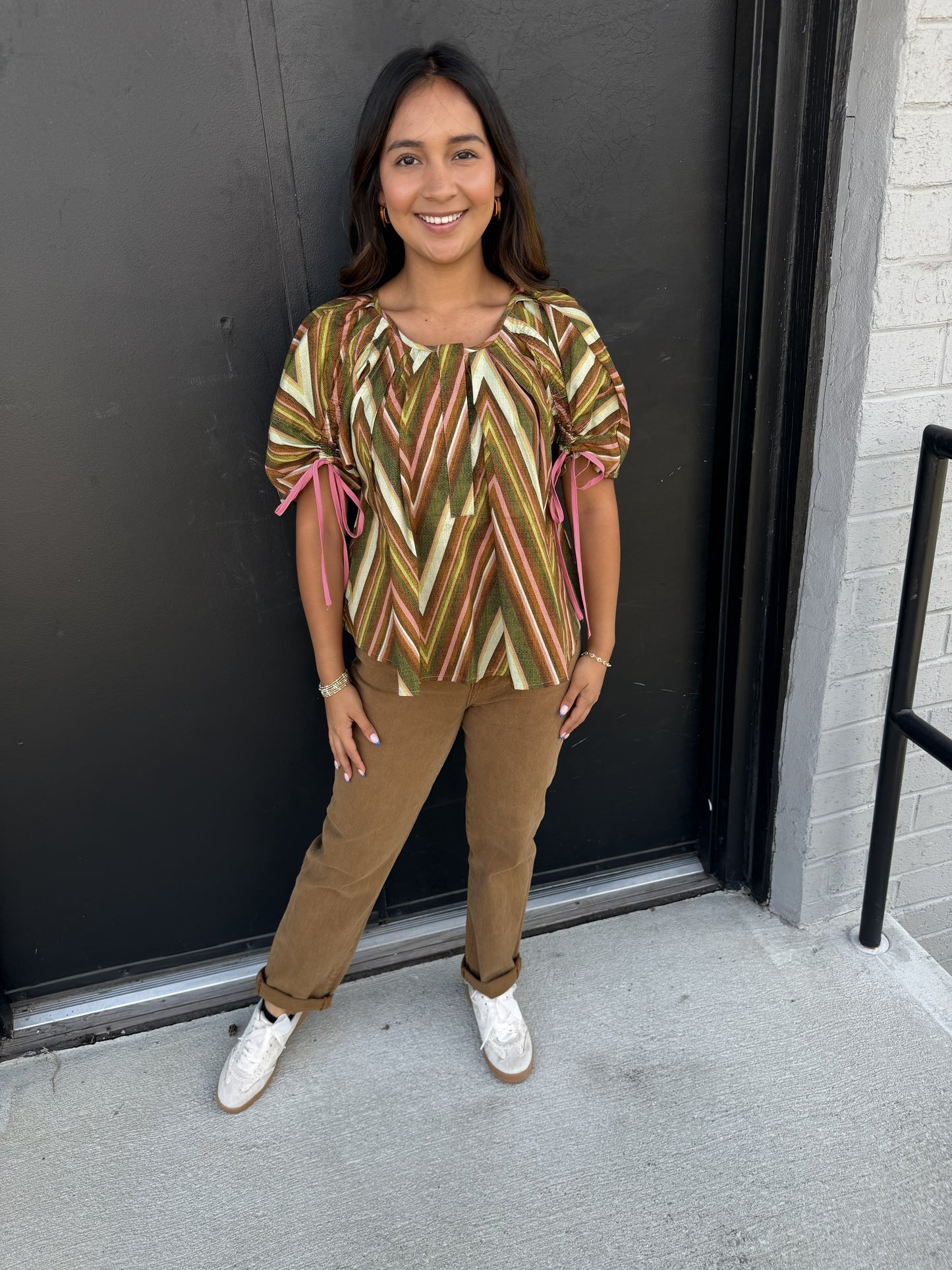 The pants are classic tan/camel-colored trousers with a polished yet relaxed feel. They feature:

Warm camel/taupe color
Mid- to high-rise waistband
Straight-leg silhouette with a comfortable, easy fit
Full-length cut with the hems casually rolled/cuffed
Clean, minimal styling with a smooth, structured appearance
Versatile neutral shade that pairs beautifully with the earthy tones in the printed top