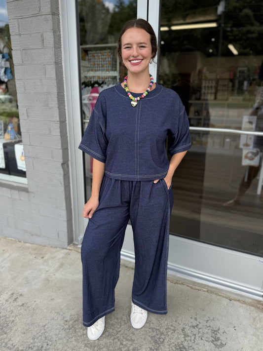 Matching deep navy wide-leg pants with an easy, flowy fit. The pants feature a comfortable elasticized waistband with a drawstring, practical side pockets, and contrast stitching down the sides and around the hem. The wide-leg silhouette creates a relaxed, coordinated look.