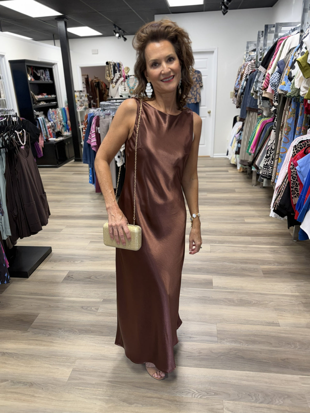 This is an elegant chocolate-brown satin maxi dress with a sleek, minimalist silhouette. It features a sleeveless design with a softly rounded bateau neckline, giving the bodice a clean and sophisticated finish.

The lustrous satin fabric drapes fluidly over the body in a relaxed, straight-to-slightly A-line shape, falling to a graceful floor-length hem. Its rich mocha/chocolate hue and subtle sheen give it a luxurious look without needing elaborate detailing. The understated design makes it especially vers