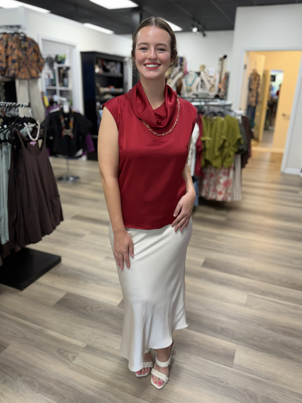 This top is an elegant deep burgundy satin blouse with a soft, lustrous finish. It features a sleeveless silhouette with extended shoulders and a beautifully draped cowl neckline that creates a sophisticated, fluid look. The relaxed, straight-cut bodice falls smoothly over the figure, while the rich wine-red color gives it a polished, dressy feel perfect for work, dinners, or special occasions.