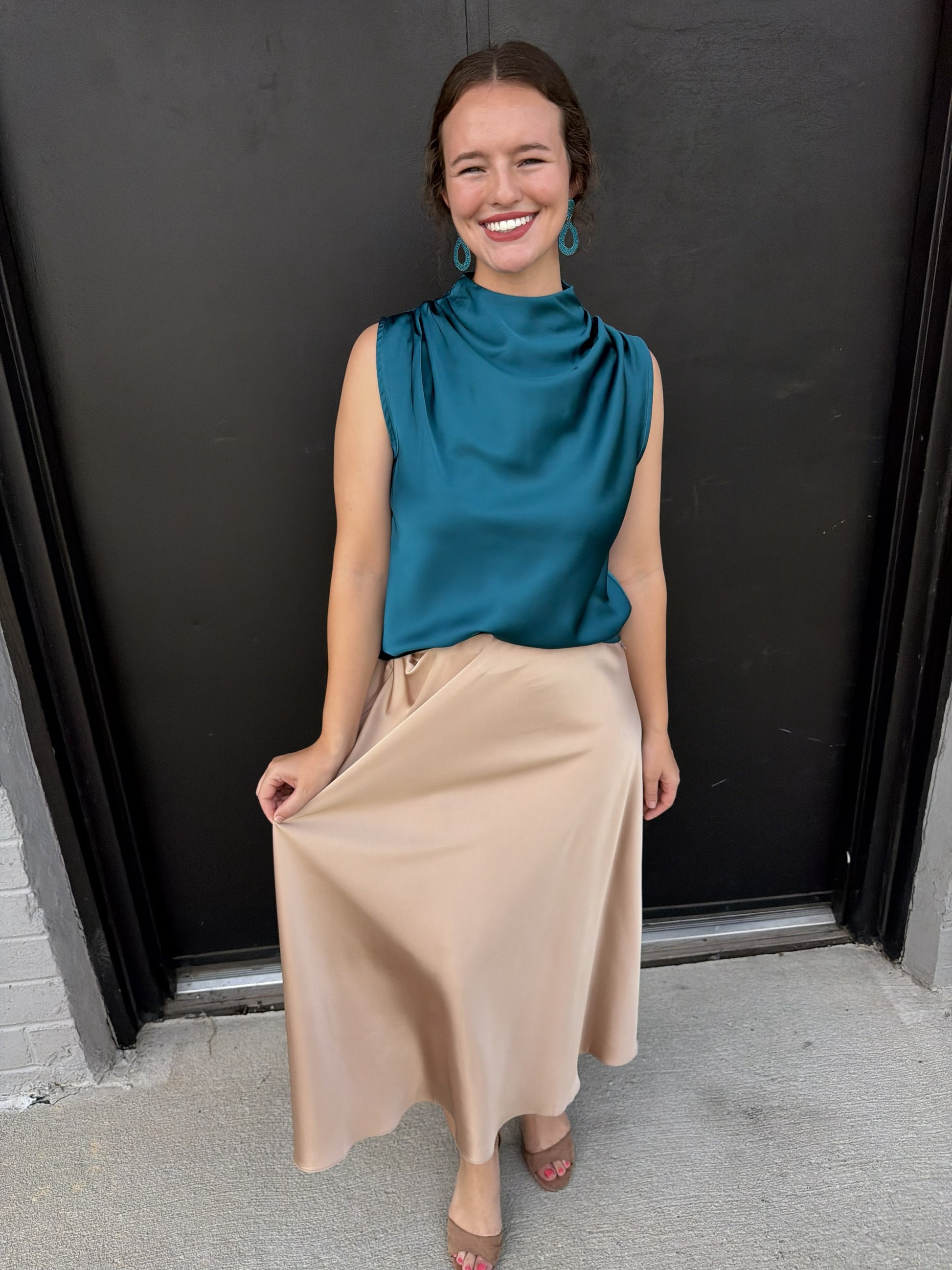 This elegant champagne-beige midi skirt has a soft, feminine drape and a polished, sophisticated feel.

Color: Warm champagne/beige
Silhouette: Fluid, gently A-line shape that skims the hips and falls loosely toward the hem
Waist: Smooth, fitted waistband with subtle gathering/pleating at the front
Length: Midi length, falling below the calf
Fabric: Smooth, lightweight fabric with a silky appearance and graceful movement
Hem: Soft, flowing hemline with a slightly asymmetrical drape as it falls naturally